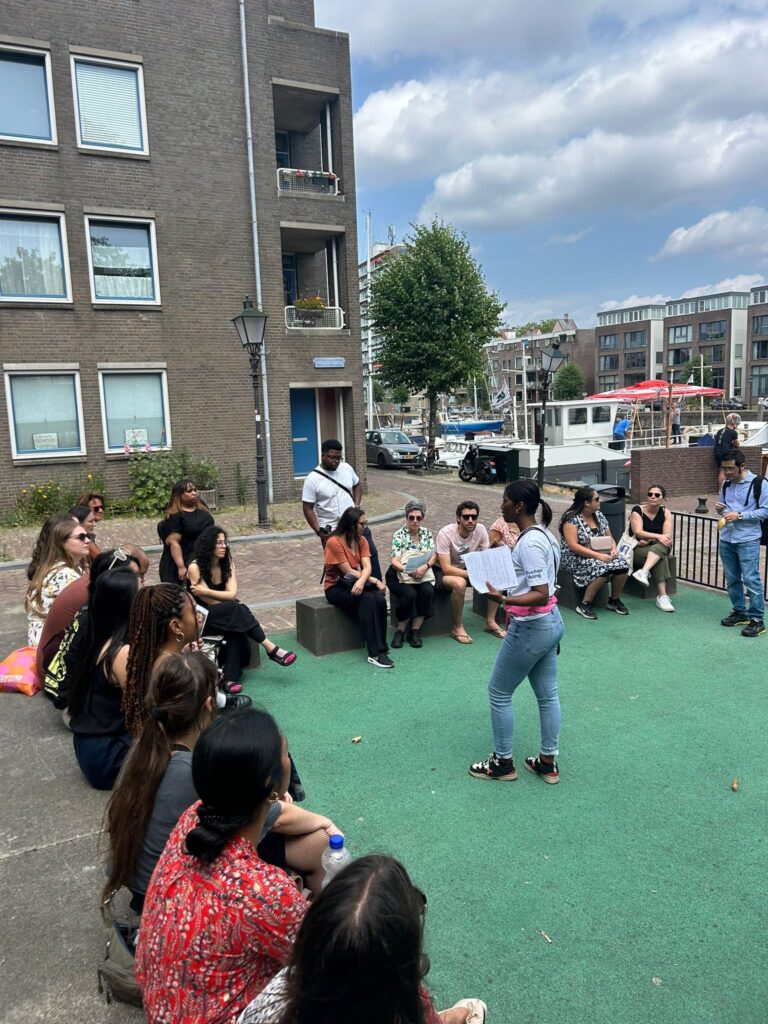 Een van de wandeltours ‘Koloniaal Delfshaven’ waarbij tourgids Annie in het midden staat en vertelt aan een groep van ruim twintig mensen.